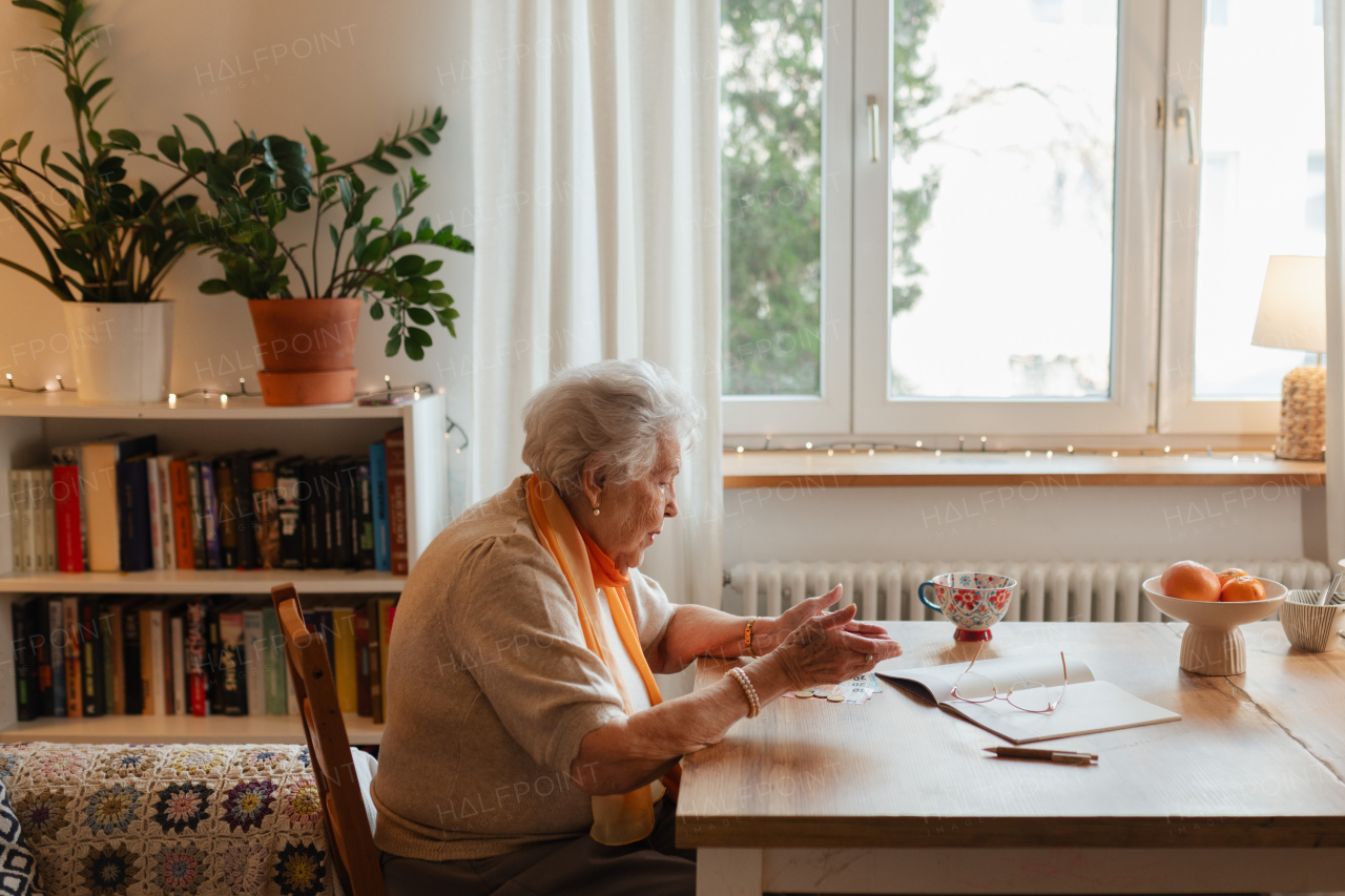 Side view of ederly woman looking sadly at few banknotes on table. Concept of financial struggles for seniors.