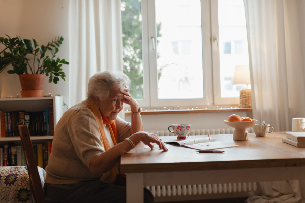 Elderly woman looking sadly at few banknotes on table. Concept of financial struggles for seniors.