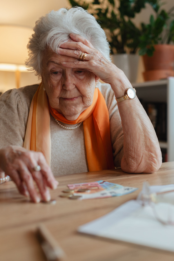 Elderly woman looking sadly at few banknotes on table. Concept of financial struggles for seniors.