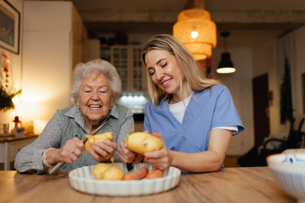 Portrait of an elderly companion assistant and senior woman peeling potatoes. Home health care services.