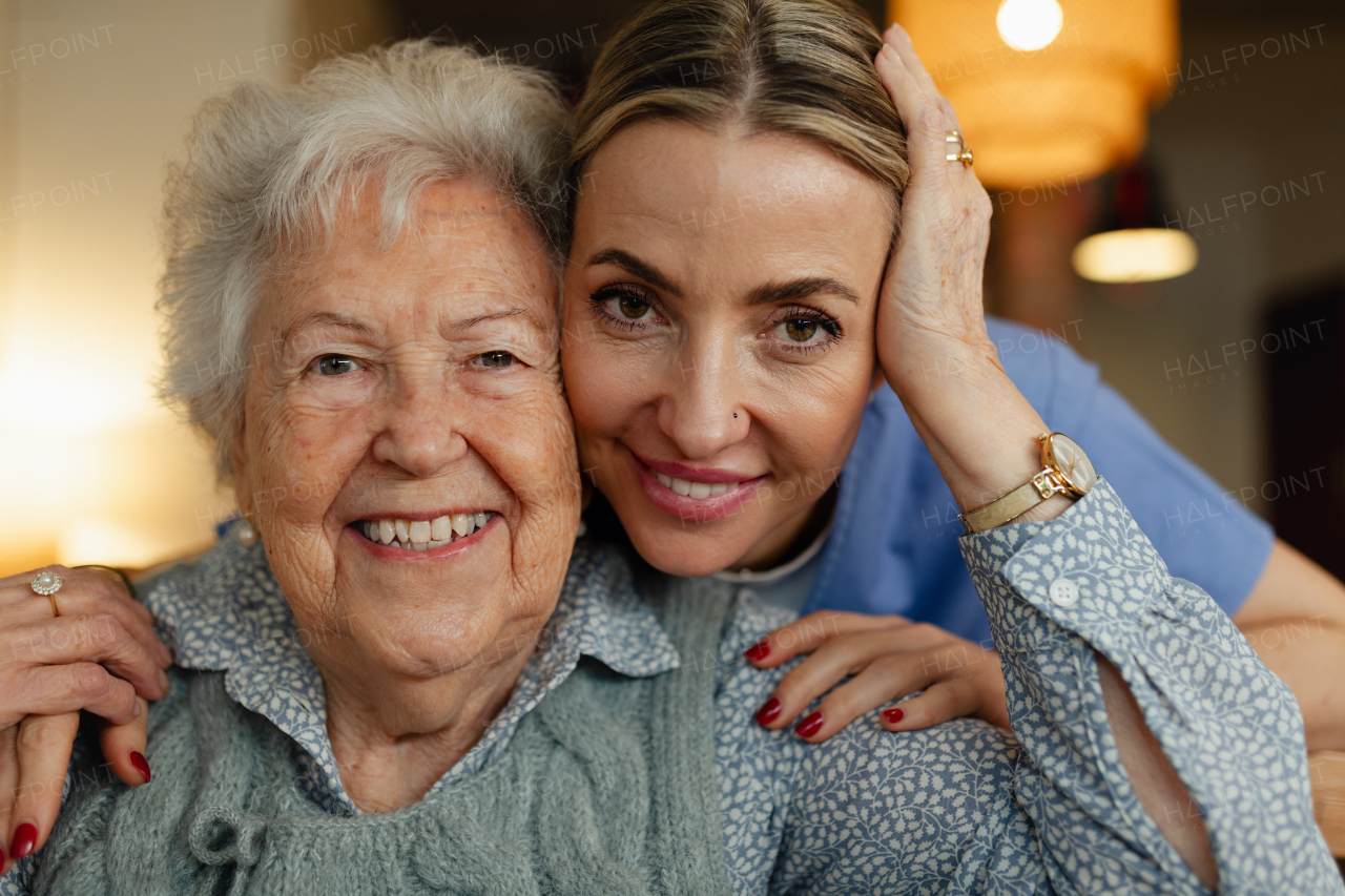 Portrait of caring healthcare worker visiting a senior patient at home, hugging her