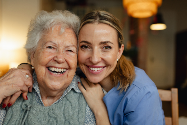 Portrait of caring healthcare worker visiting a senior patient at home, hugging her