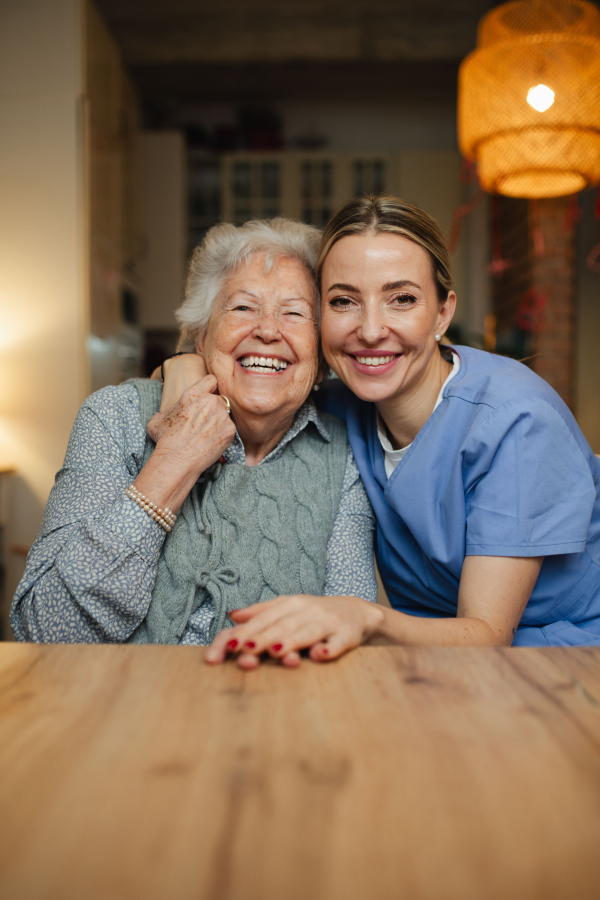 Portrait of caring healthcare worker visiting a senior patient at home, hugging her