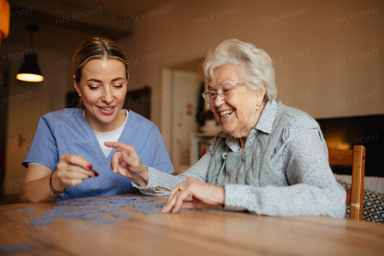 Friendly caregiver and elderly patient working on puzzle together, having fun. Home health care services.