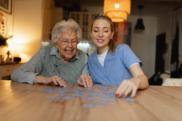 Friendly caregiver and elderly patient working on puzzle together, having fun. Home health care services.