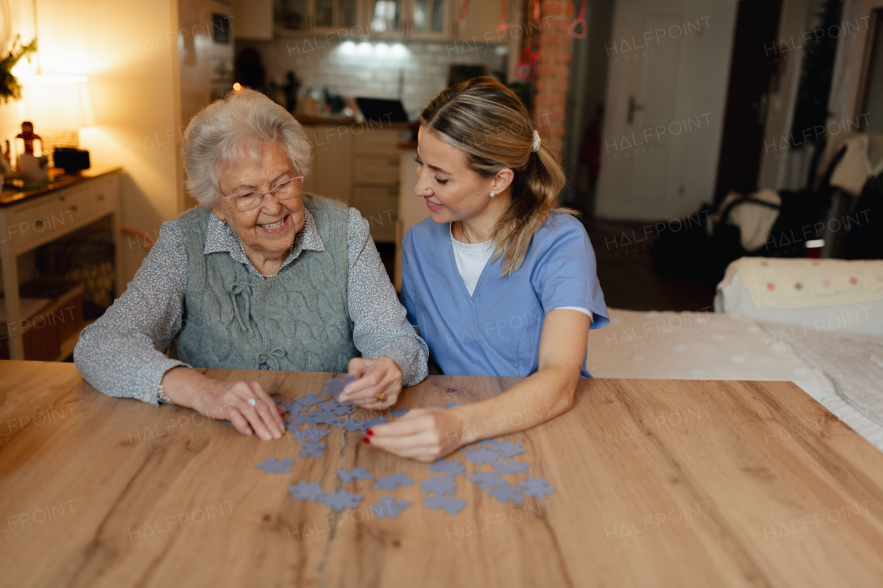 Friendly caregiver and elderly patient working on puzzle together, having fun. Home health care services.