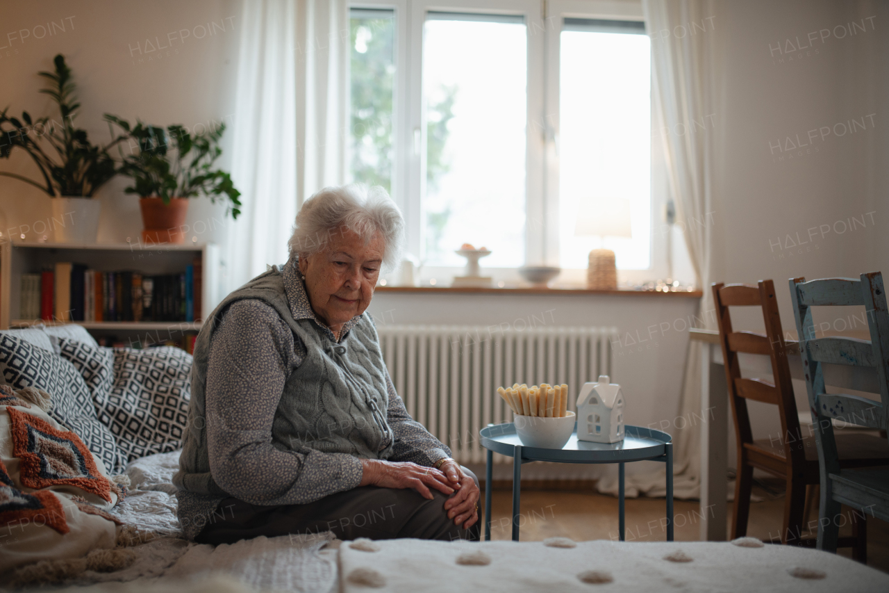 Senior woman living alone and feeling lonely. Portrait of senior woman sitting on sofa at home.