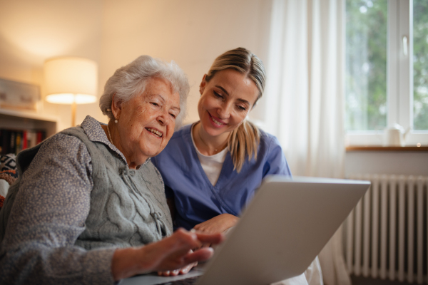 Social worker helping elderly lady with managing her finances and teaching her to use laptop.