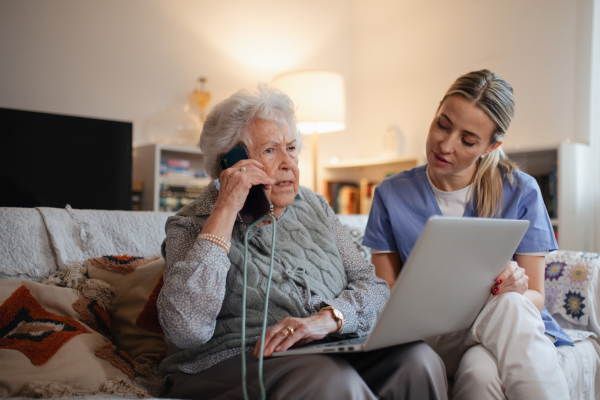 Caregiver helping elderly lady with managing her finances and teaching her to use online banking on laptop.