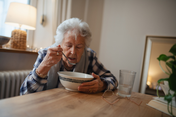 Poor and lonely elderly woman eating soup at the dining table.