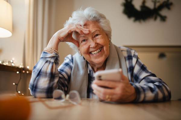 Elderly woman feeling confident while using smartphone, sitting in the kitchen.