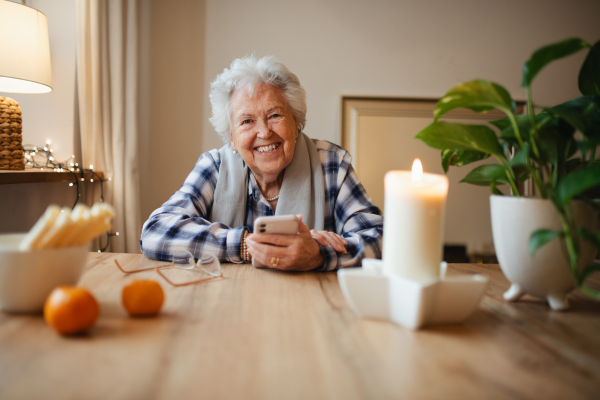 Elderly woman feeling confident while using smartphone, sitting in the kitchen.