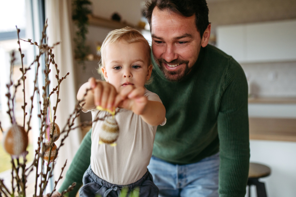 Father and little son decorating pussy willows branches, putting easter eggs on them. Concept of easter holidays.