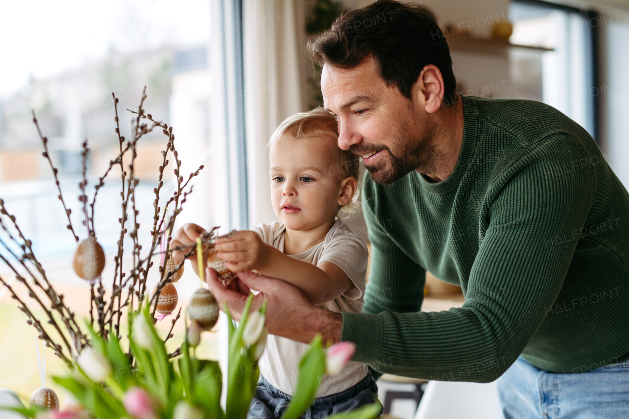 Father and little son decorating pussy willows branches, putting easter eggs on them. Concept of easter holidays.