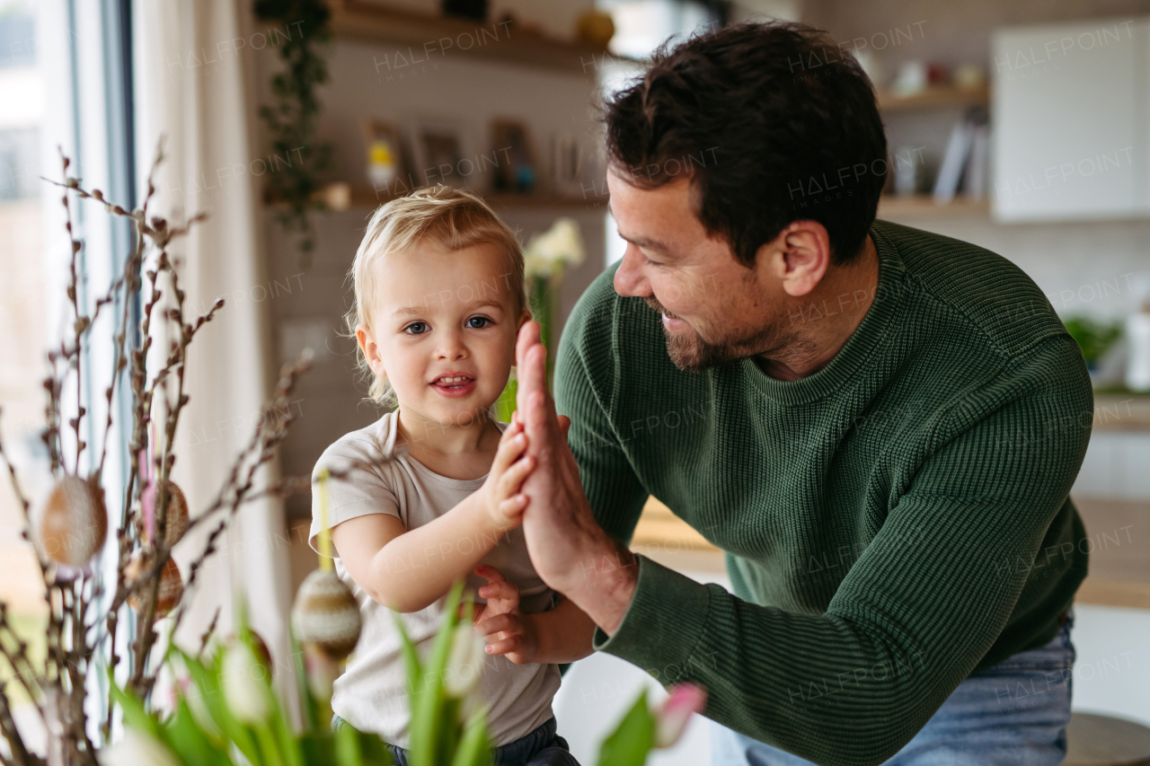 Father and little son decorating pussy willows branches, putting easter eggs on them. Concept of easter holidays.