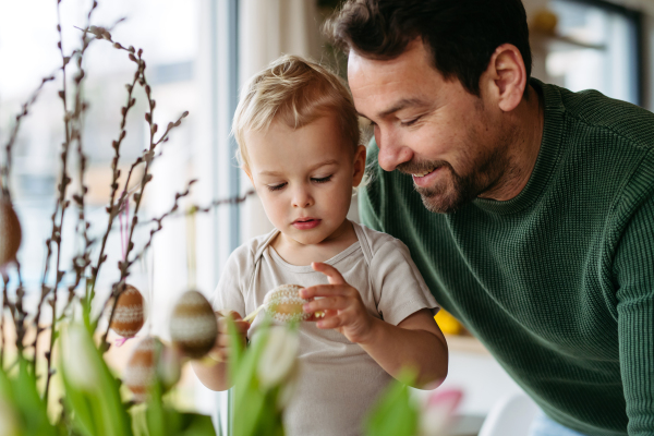 Father and little son decorating pussy willows branches, putting easter eggs on them. Concept of easter holidays.