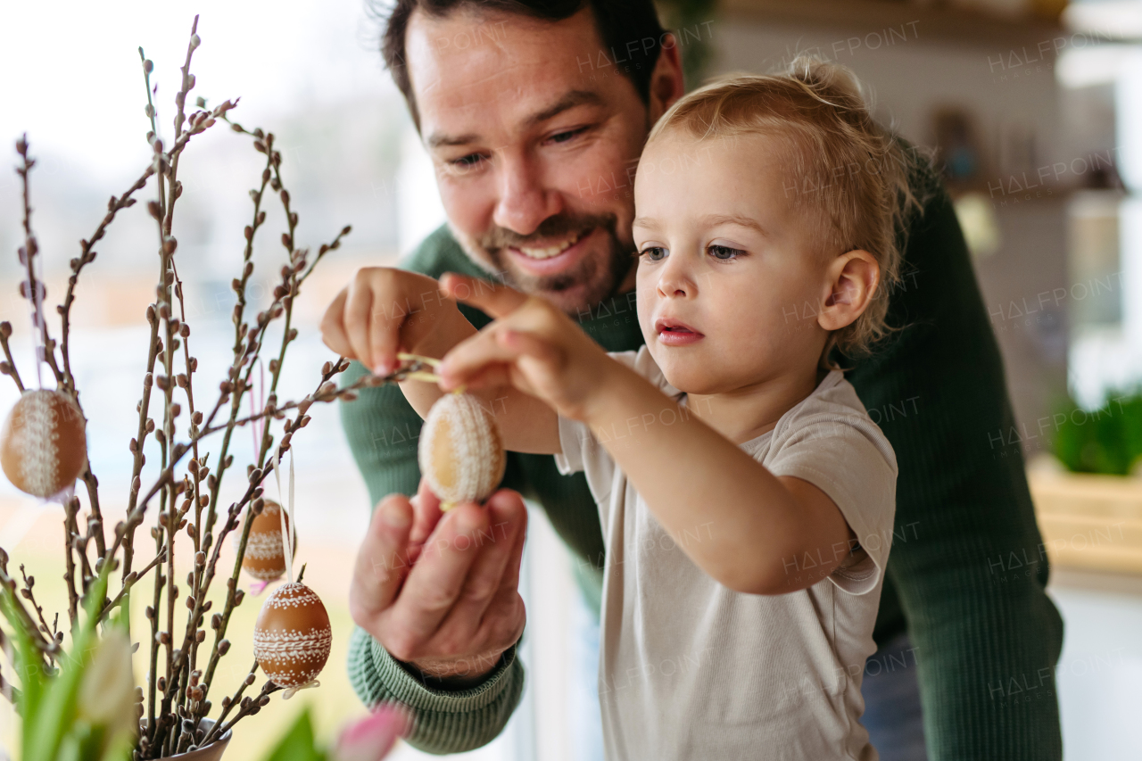 Father and little son decorating pussy willows branches, putting easter eggs on them. Concept of easter holidays.