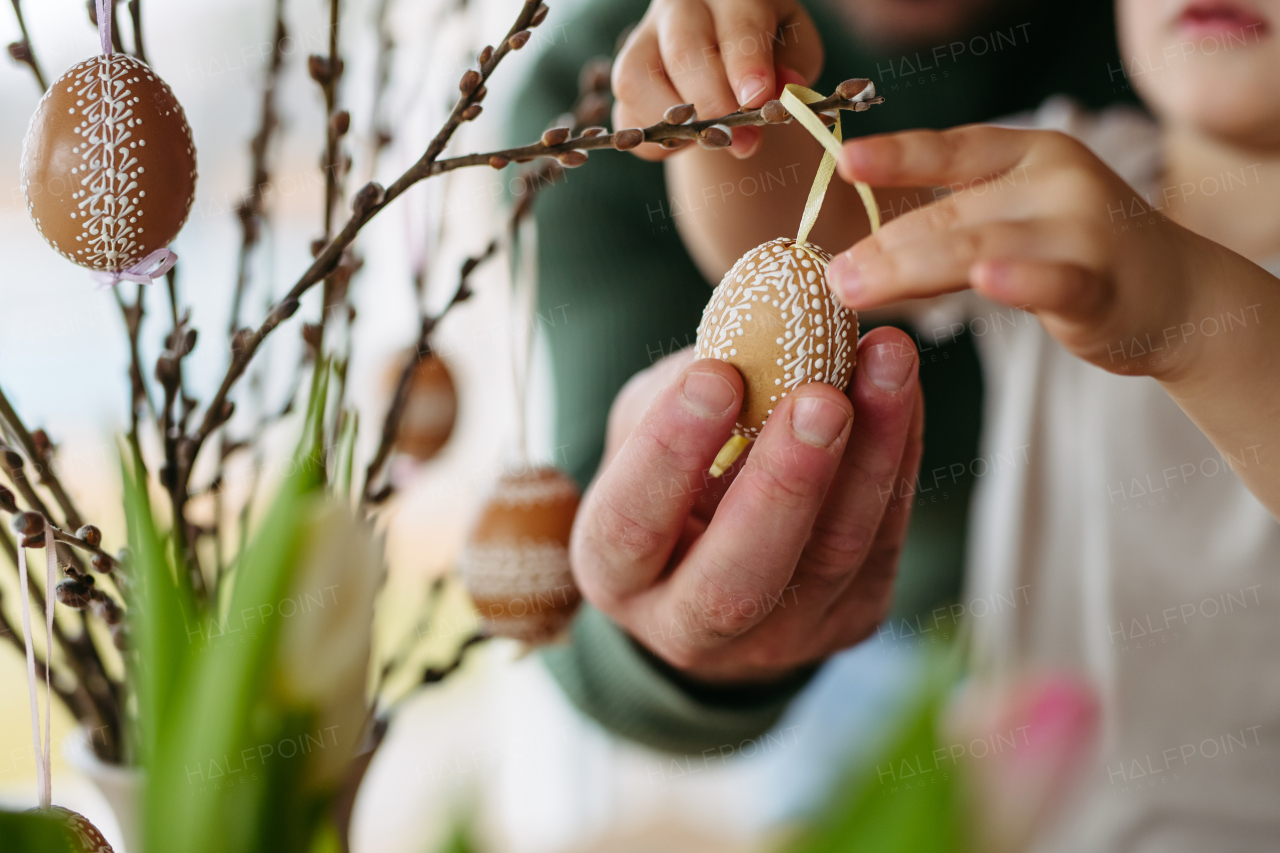 Father and little son decorating pussy willows branches, putting easter eggs on them. Concept of easter holidays.