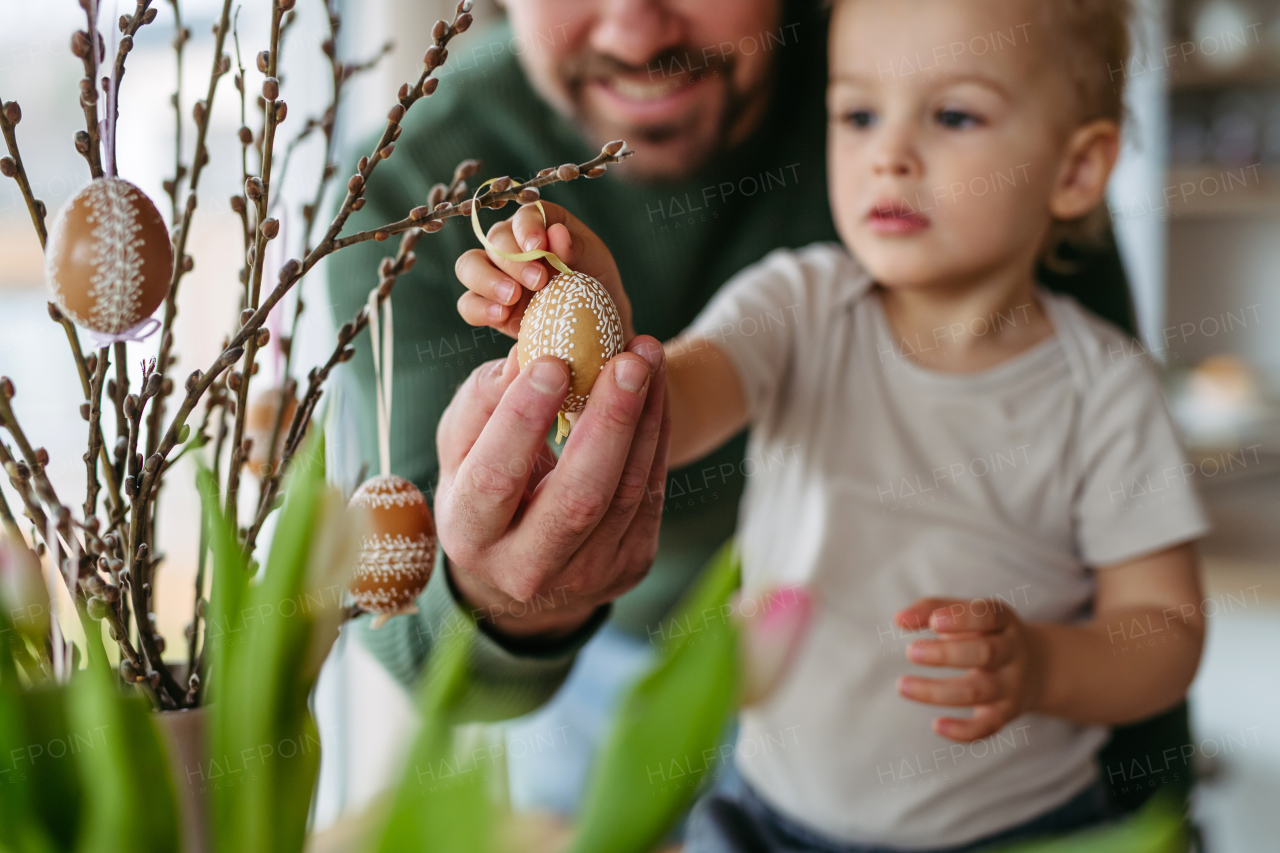 Father and little son decorating pussy willows branches, putting easter eggs on them. Concept of easter holidays.