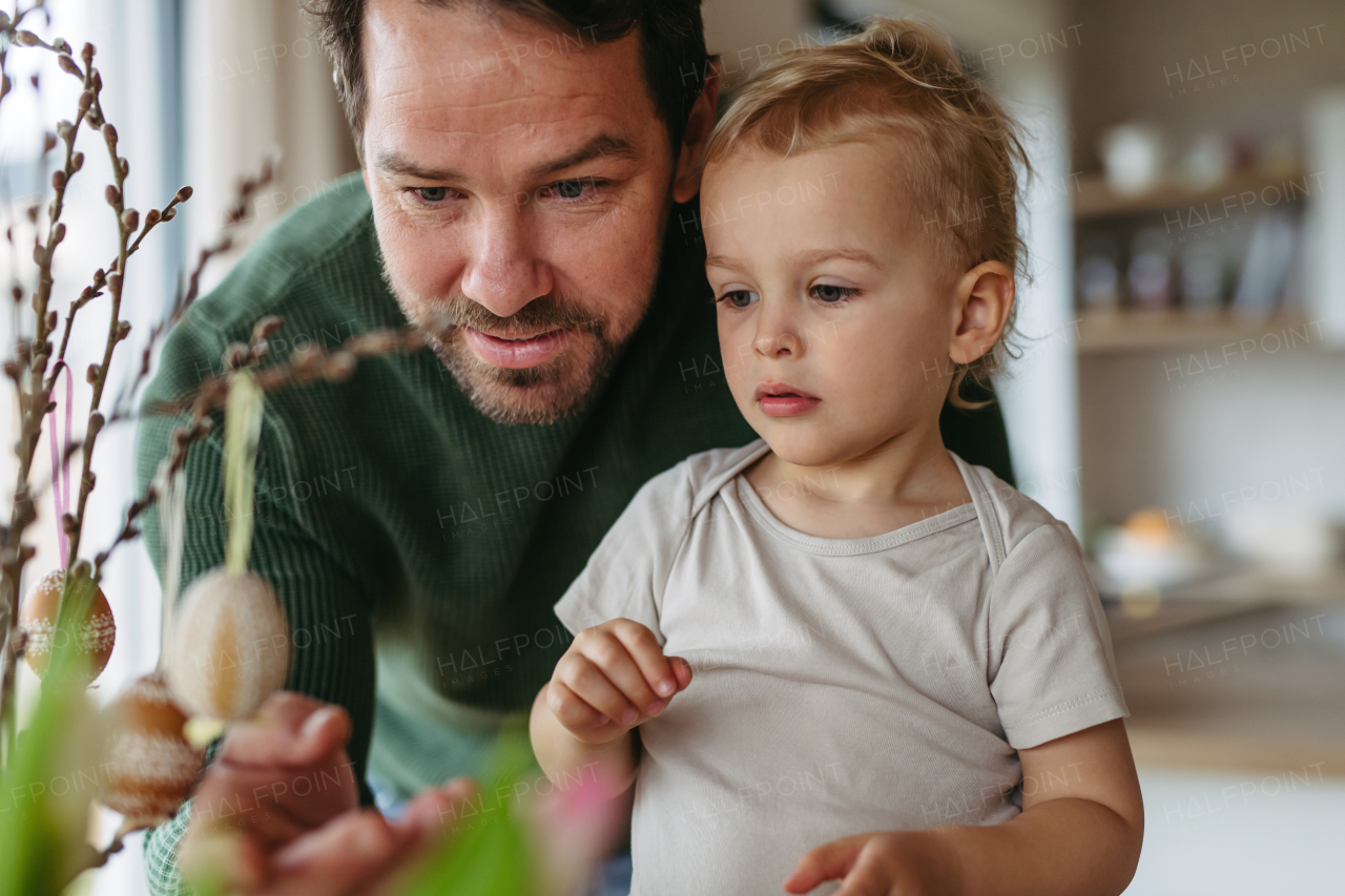 Father and little son decorating pussy willows branches, putting easter eggs on them. Concept of easter holidays.