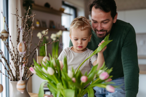 Father and little son arranging tulips in a vase. Concept of easter holidays.