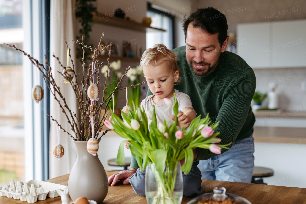 Father and little son decorating pussy willows branches, putting easter eggs on them. Concept of easter holidays.