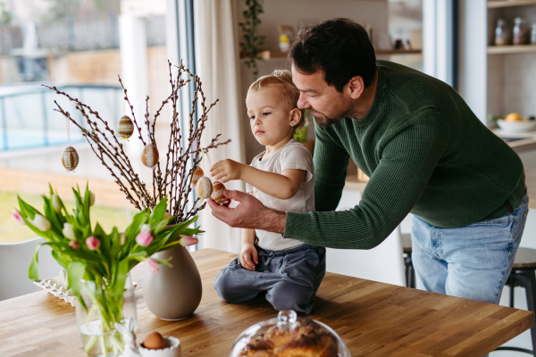 Father and little son decorating pussy willows branches, putting easter eggs on them. Concept of easter holidays.