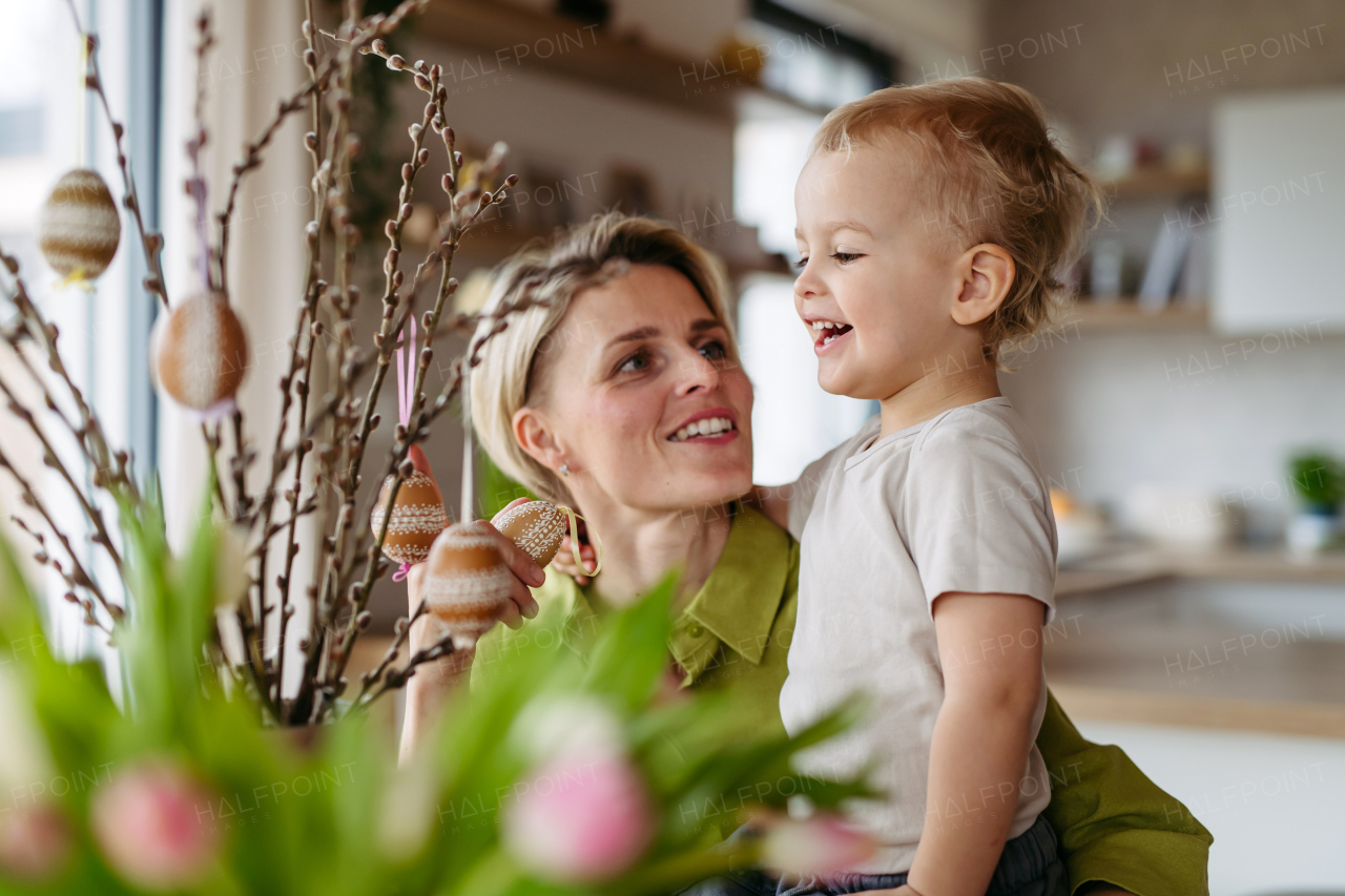 Mother and little son decorating pussy willows branches, putting easter eggs on them. Concept of easter holidays.