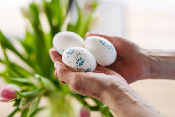 Hands holding decorated Easter eggs with traditional patterns, surrounded by festive spring elements.