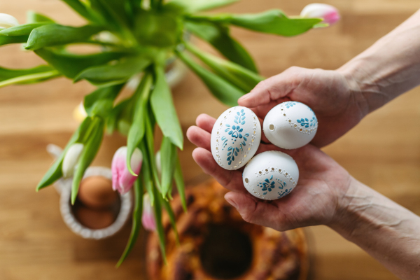 Hands holding decorated Easter eggs with traditional patterns, surrounded by festive spring elements.