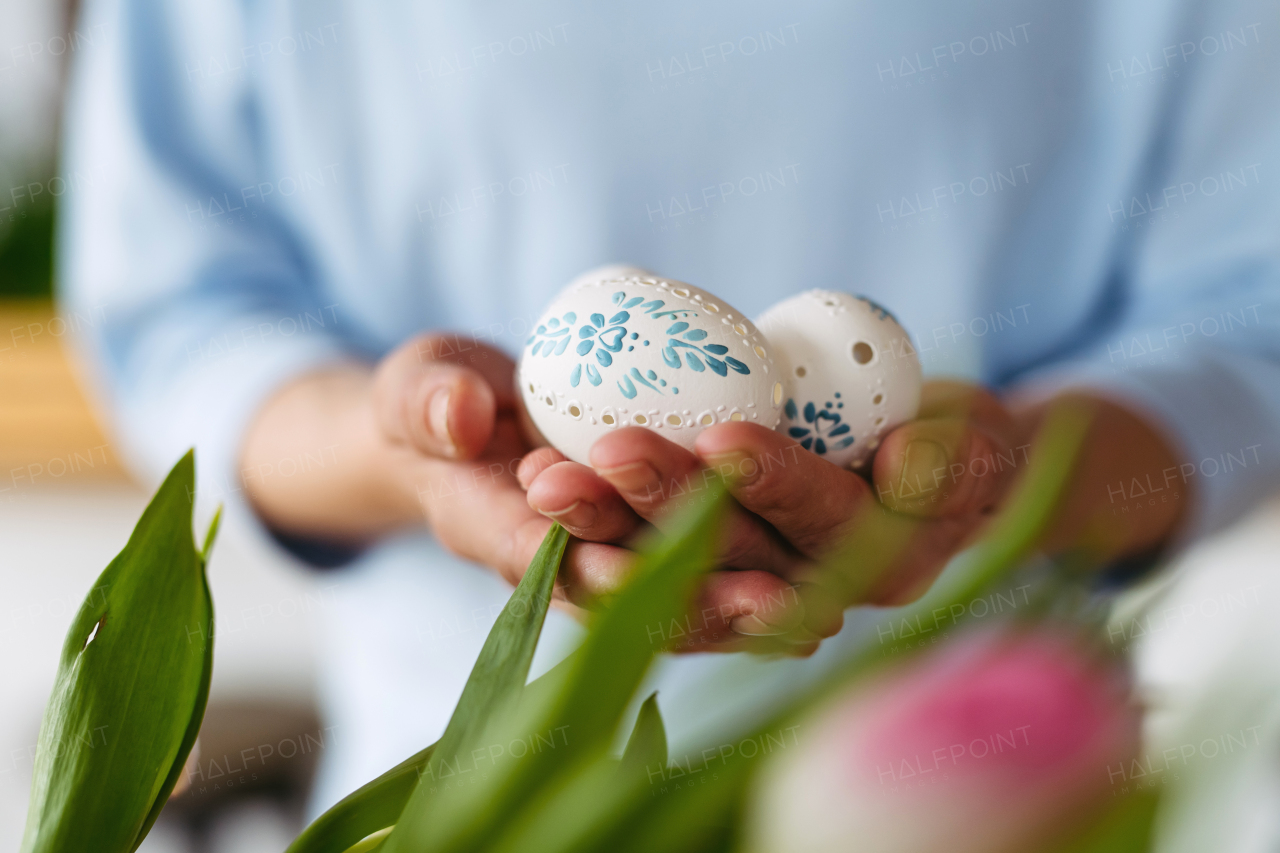 Hands holding decorated Easter eggs with traditional patterns, surrounded by festive spring elements.