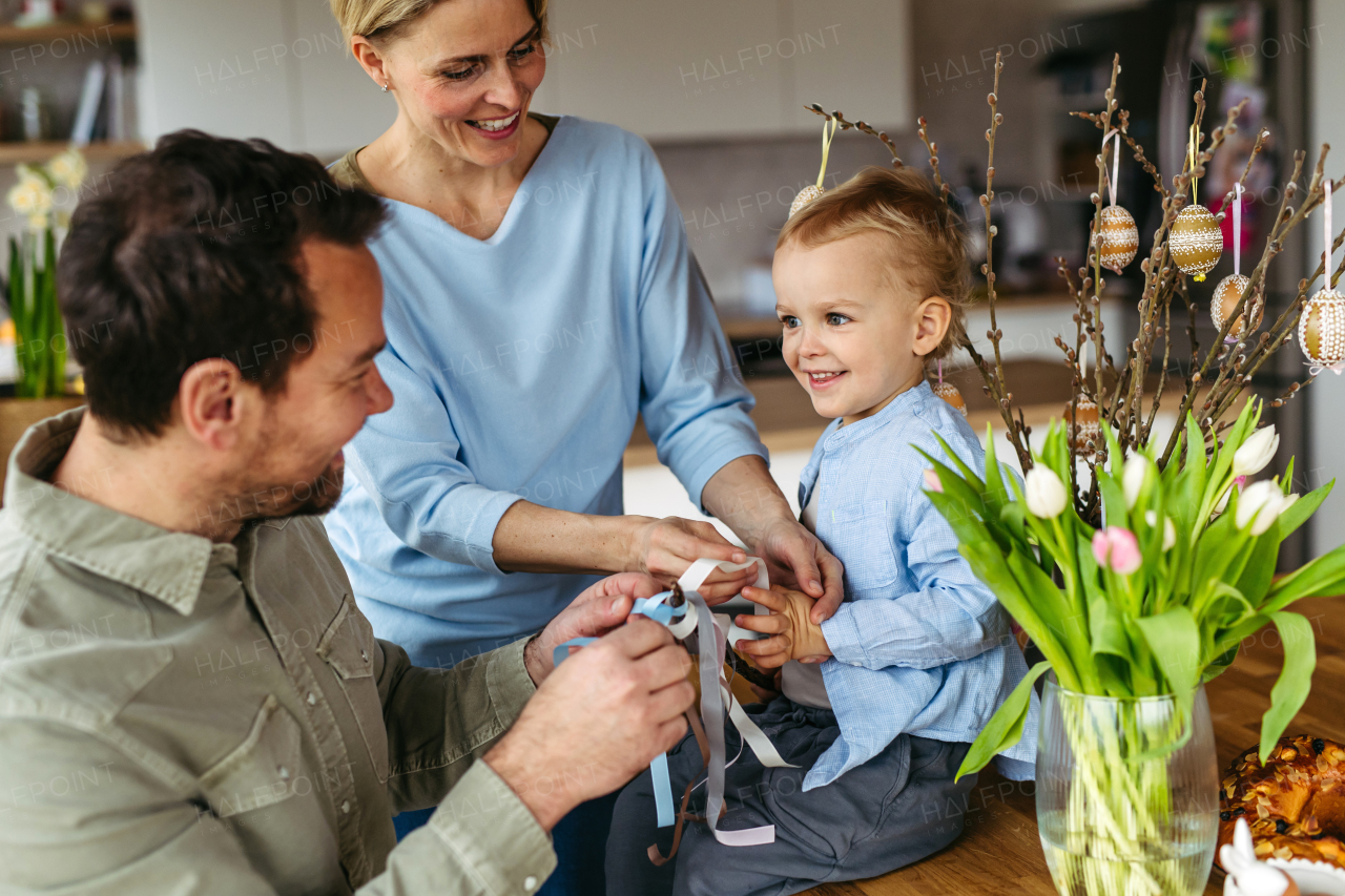 Parents helping little boy to decorate easter whip from willow branches with ribbons.