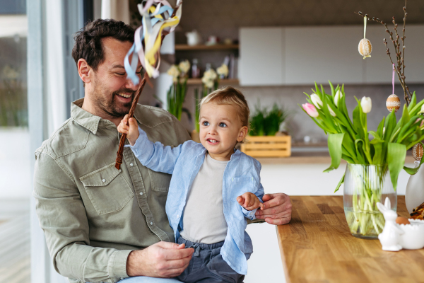 Father and little boy holding easter whip from willow branches, decorated with ribbons. Easter tradition concept.