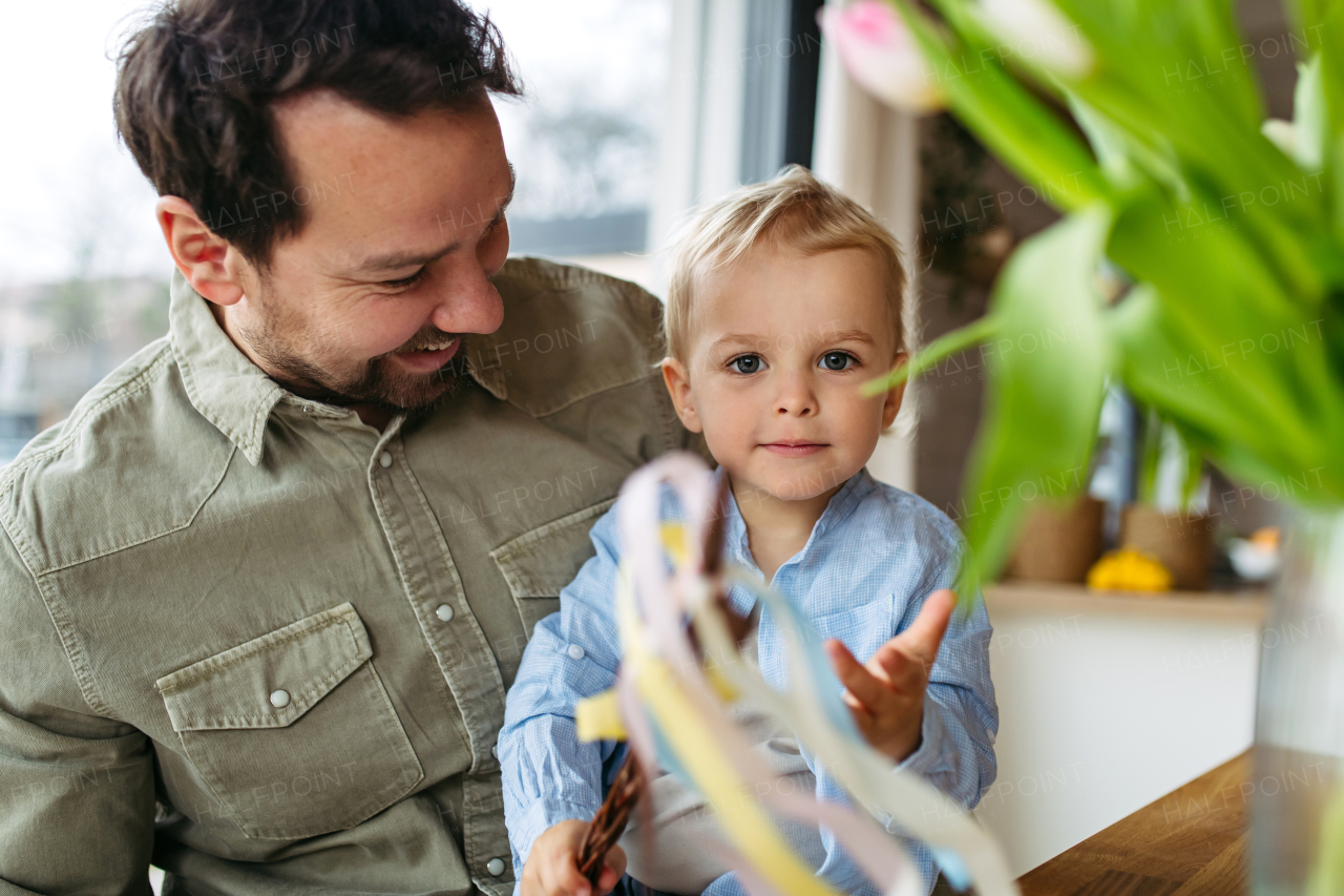 Father and little boy holding easter whip from willow branches, decorated with ribbons. Easter tradition concept.