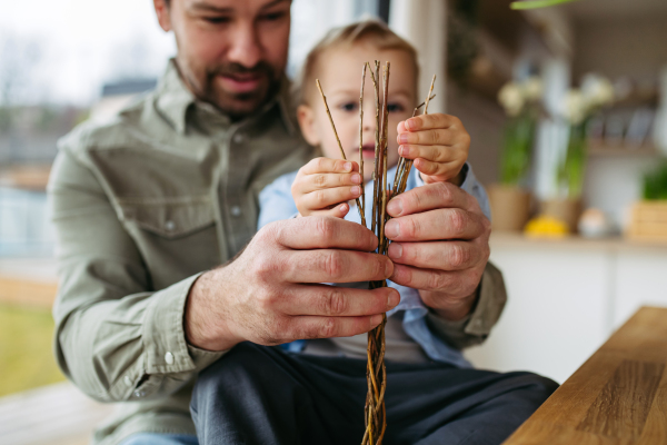 Father and little boy braiding easter whip from willow branches.