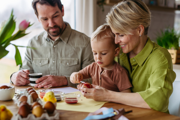 Family decorating easter eggs at home. Little boy painting eggs with brush and easter egg dye.