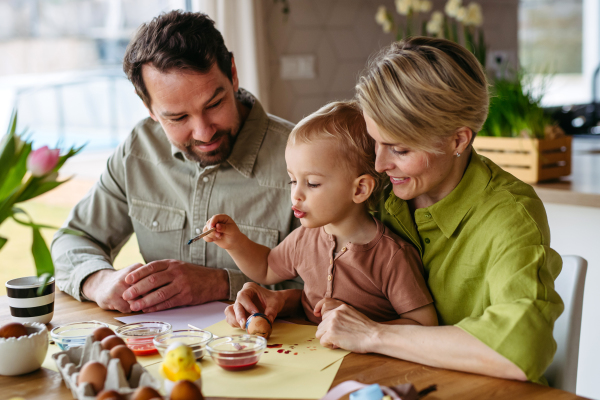 Family decorating easter eggs at home. Little boy painting eggs with brush and easter egg dye.