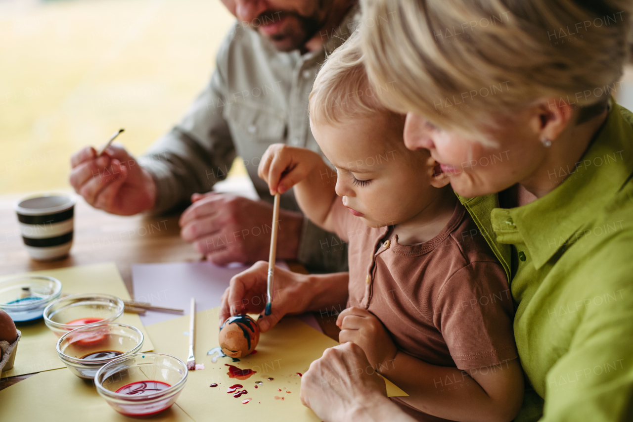 Family decorating easter eggs at home. Little boy painting eggs with brush and easter egg dye.