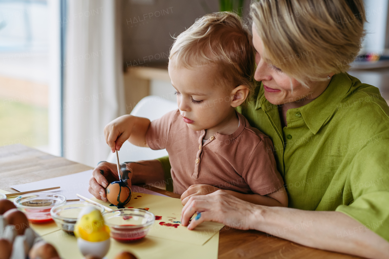 Mother and little son decorating easter eggs at home. Little boy painting eggs with brush and easter egg dye.