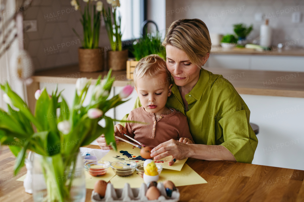 Mother and little son decorating easter eggs at home. Little boy painting eggs with brush and easter egg dye.