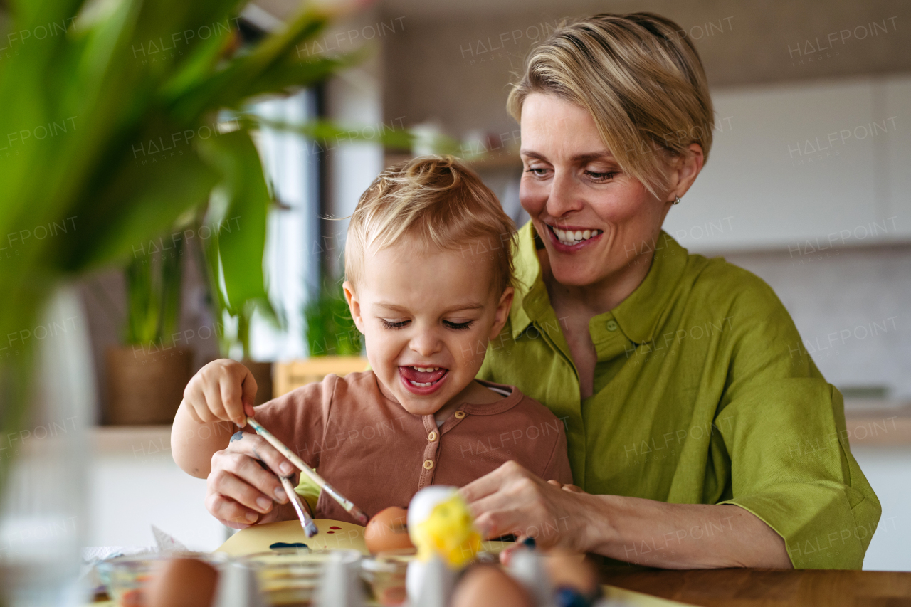 Mother and little son decorating easter eggs at home. Little boy painting eggs with brush and easter egg dye.