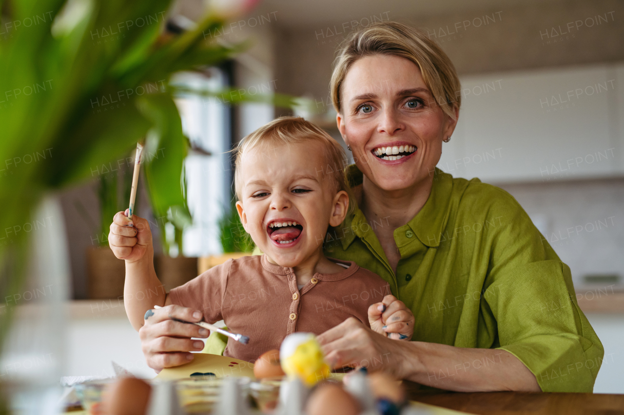 Mother and little son decorating easter eggs at home. Little boy painting eggs with brush and easter egg dye.