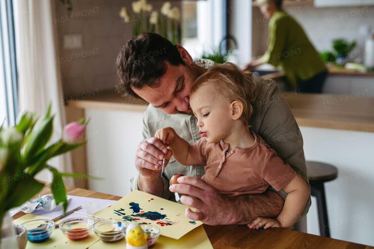 Father and little son decorating easter eggs at home. Little boy painting eggs with brush and easter egg dye.