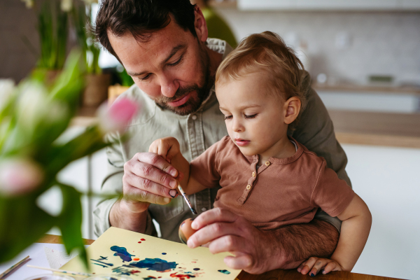 Father and little son decorating easter eggs at home. Little boy painting eggs with brush and easter egg dye.