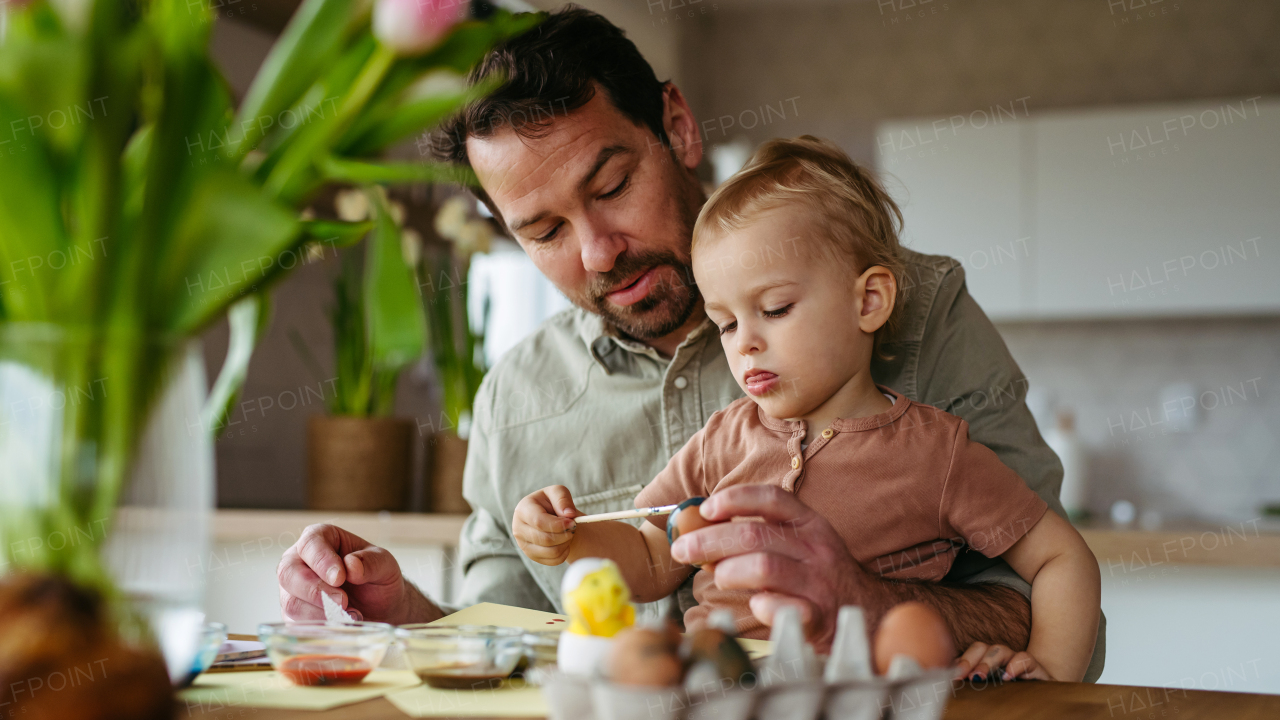 Father and little son decorating easter eggs at home. Little boy painting eggs with brush and easter egg dye.