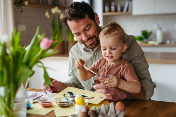 Father and little son decorating easter eggs at home. Little boy painting eggs with brush and easter egg dye.