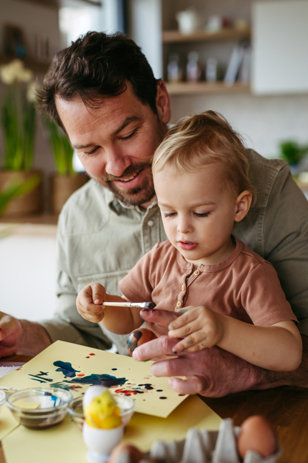 Father and little son decorating easter eggs at home. Little boy painting eggs with brush and easter egg dye.