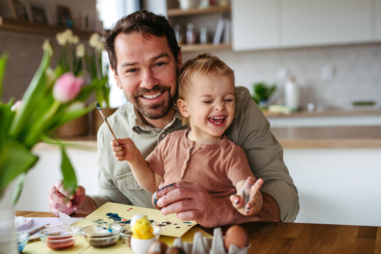 Father and little son decorating easter eggs at home. Little boy painting eggs with brush and easter egg dye.