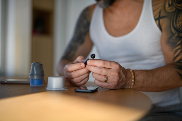 Close up of diabetic man preparing blood glucose meter to check blood sugar at home.