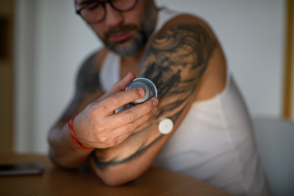 Close up of diabetic man using sensor applicator to insert the CGM sensor into his arm.